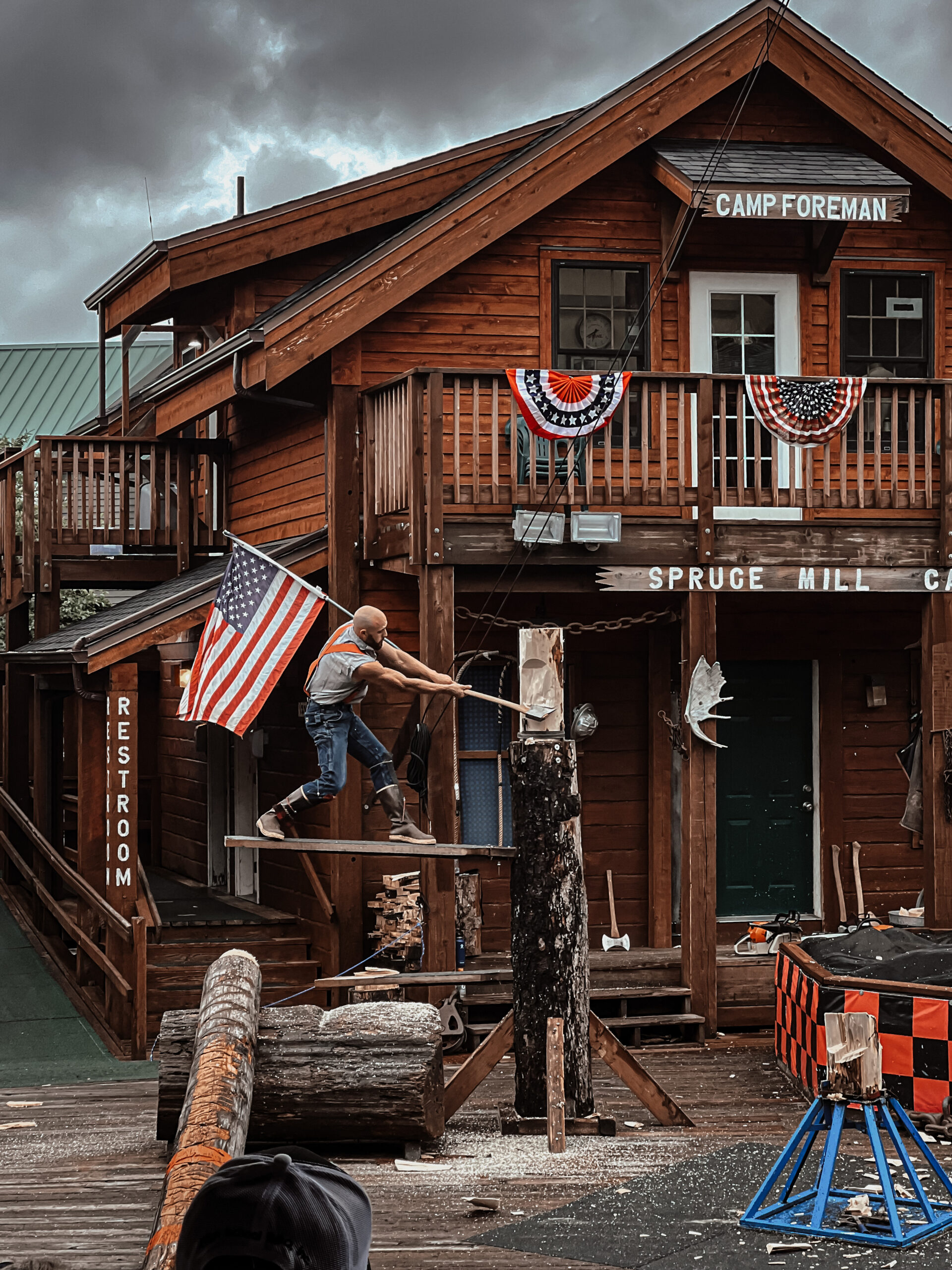 A lumberjack from The Great Alaskan Lumberjack show showcasing his strength by splitting a tree trunk with an ax while balancing on a thin piece of wood serving as a parapet. This attraction is a great choice for visitors, which is why it's been included in this travel guide for Ketchikan.